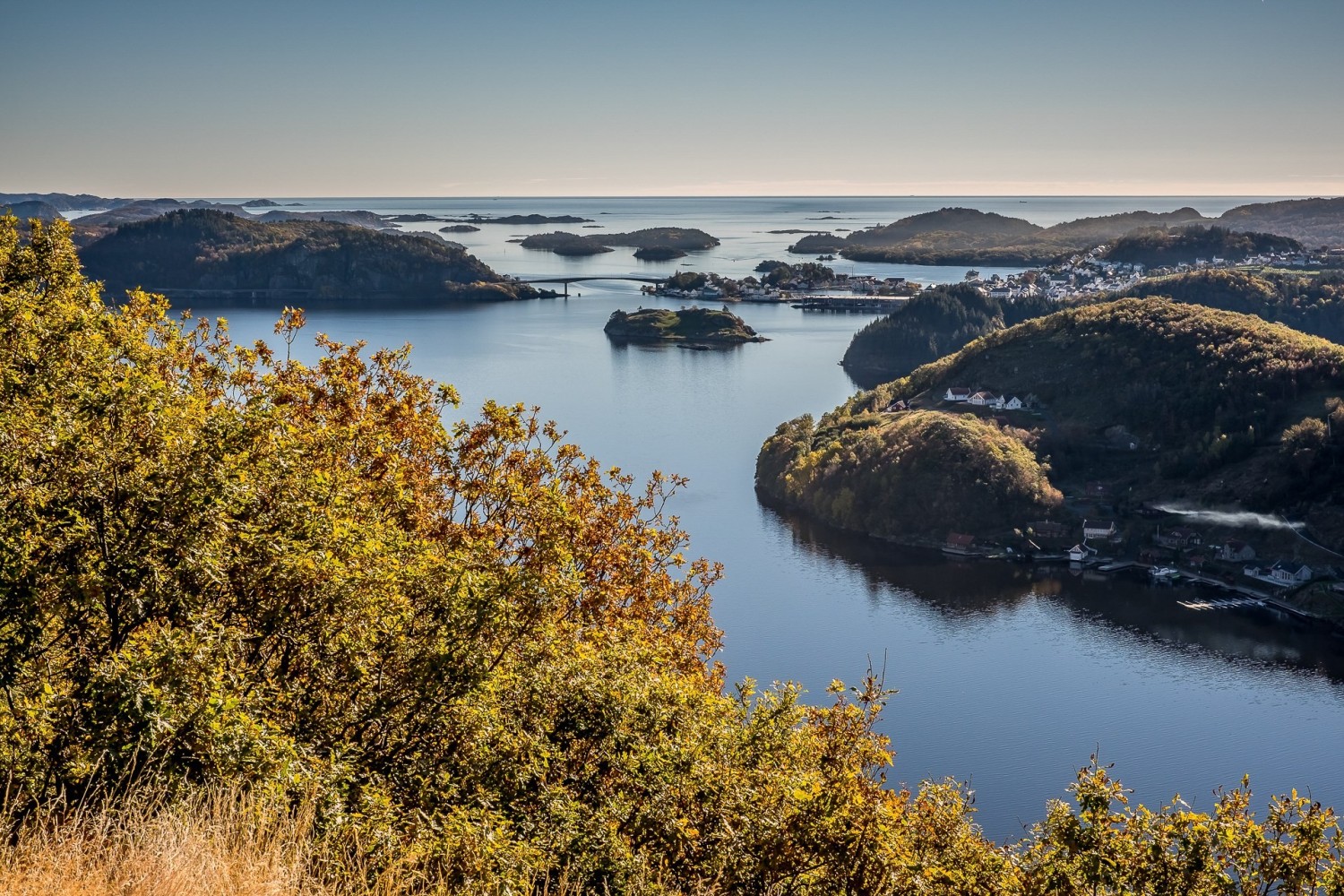 Utsikt over fjorden og skjærgården ved Farsund, med høstfargede trær i forgrunnen og Farsund by synlig i bakgrunnen.