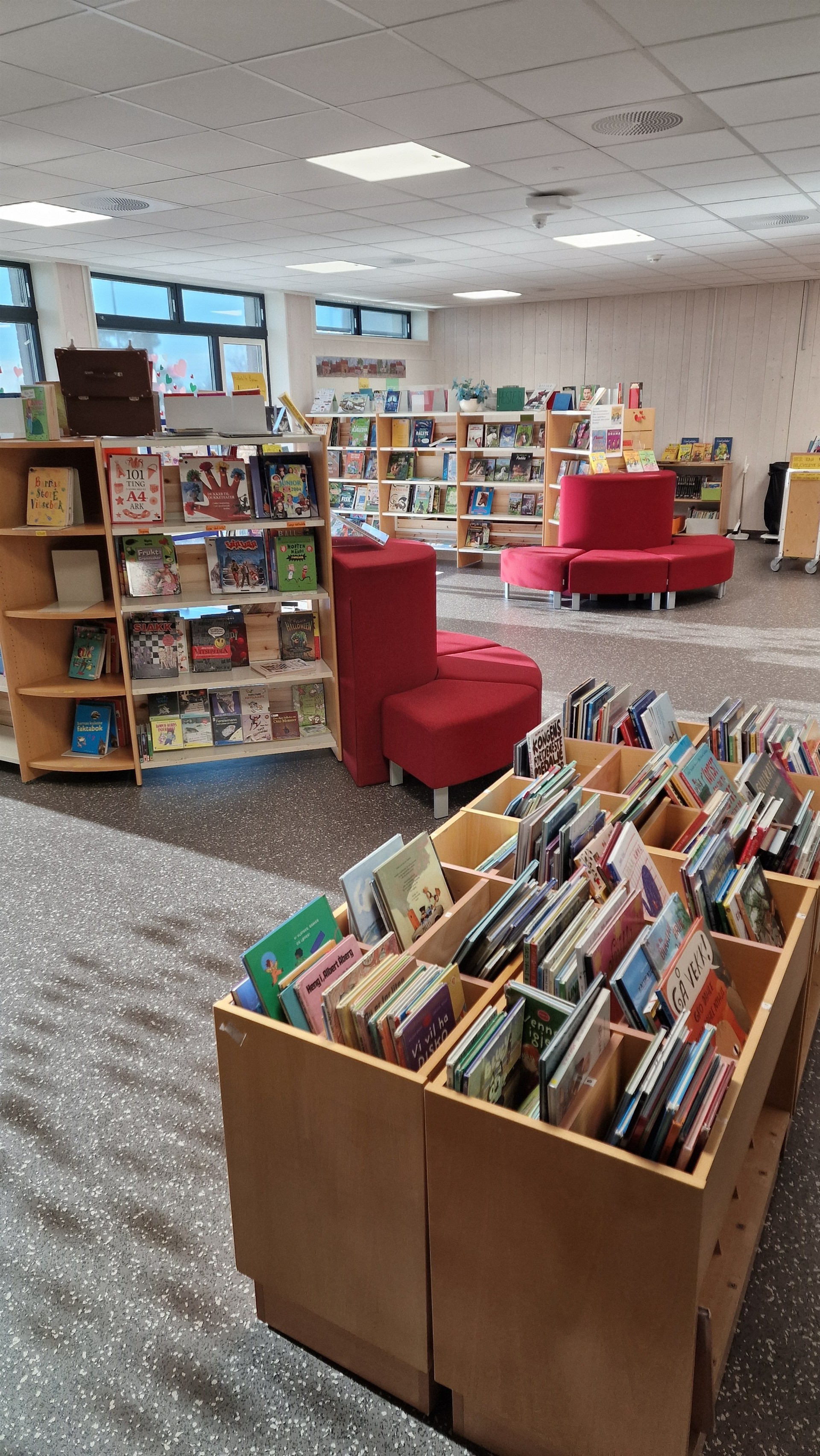 Bilde av innsiden av biblioteket ved Farsund barneskole. Nærmest i bildet kan man se bøker i bokkasse, og i bakgrunnen bokhyller og røde sitteputer.