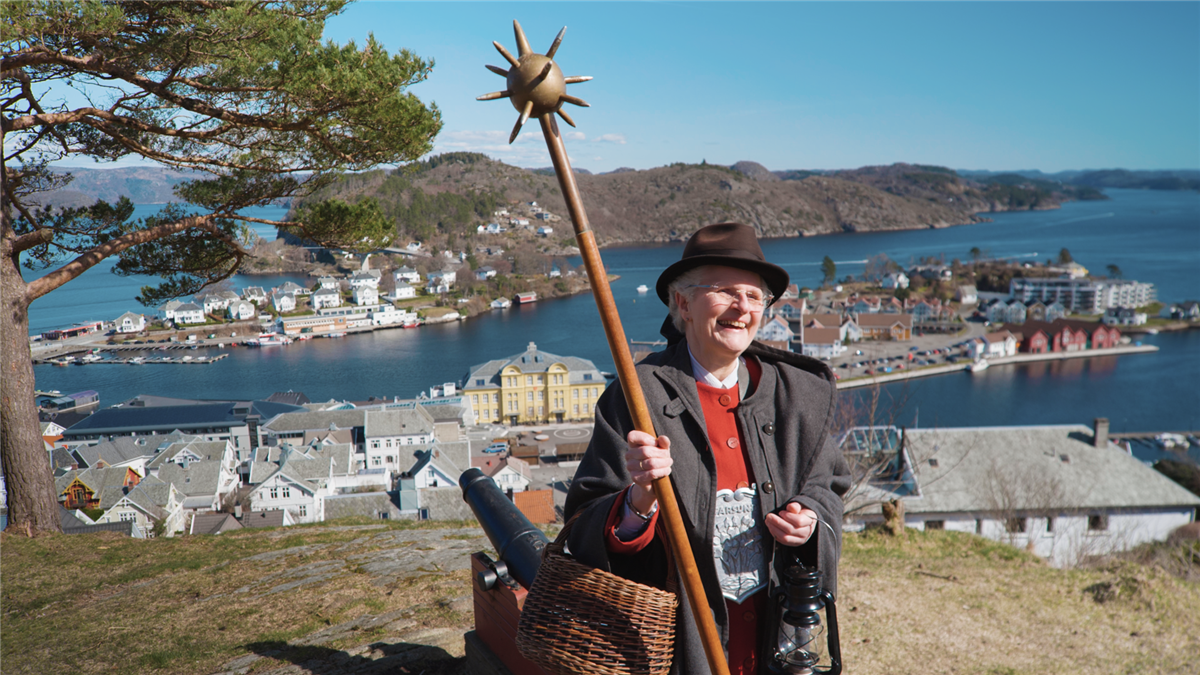 Elin står på Varbakk med Farsund i bakgrunnen og holder vekterstav - Klikk for stort bilde